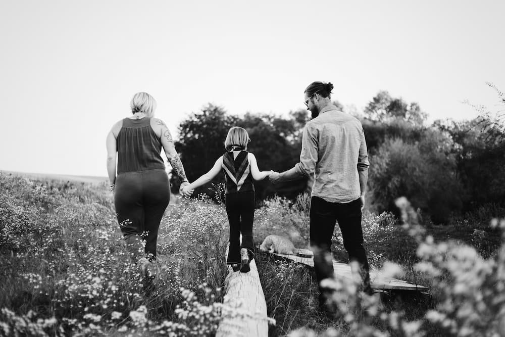 A black and white photo of parents and a child in field walking on a log