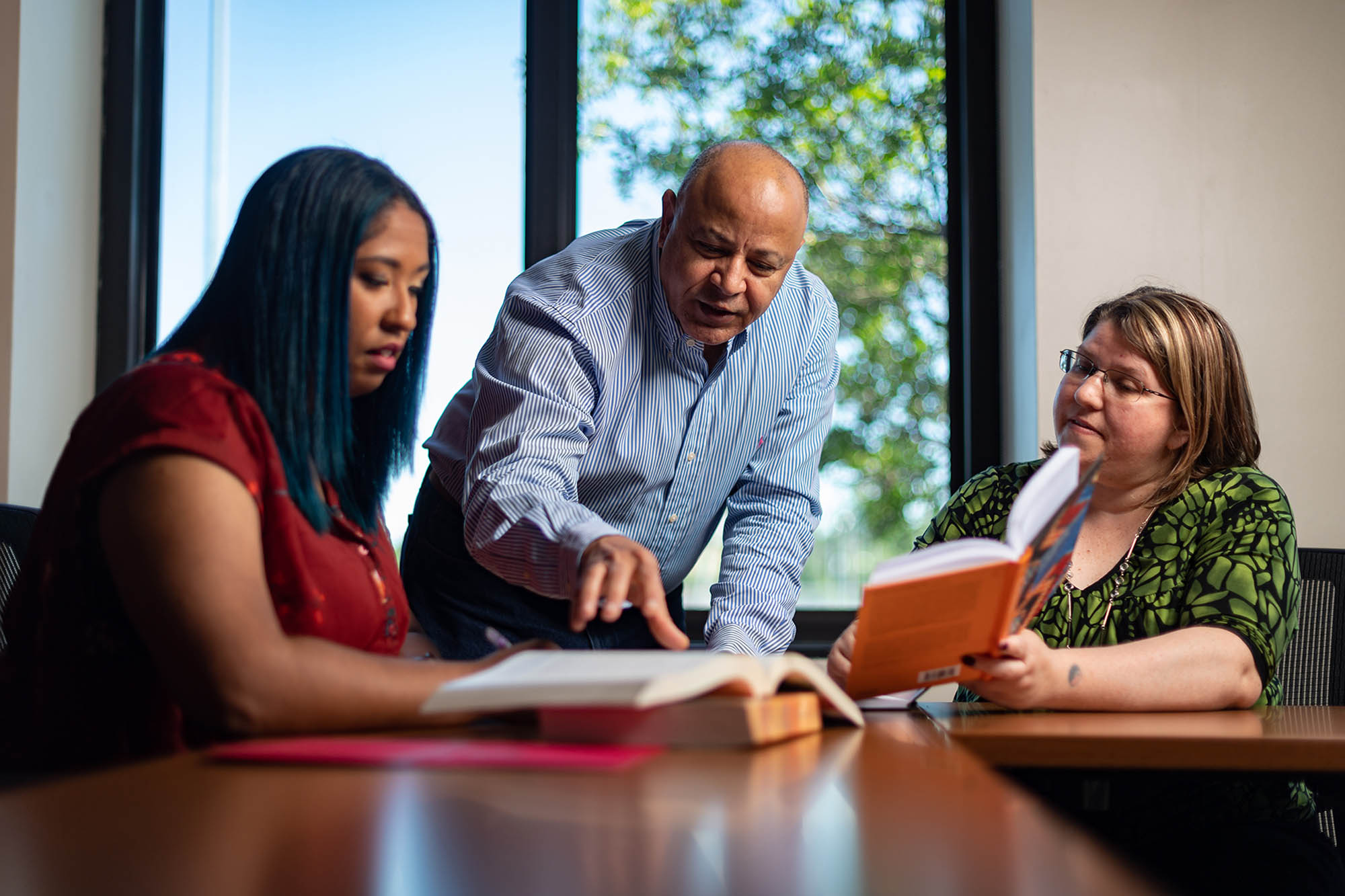 three adults sit in a collaboration space and look over a textbook