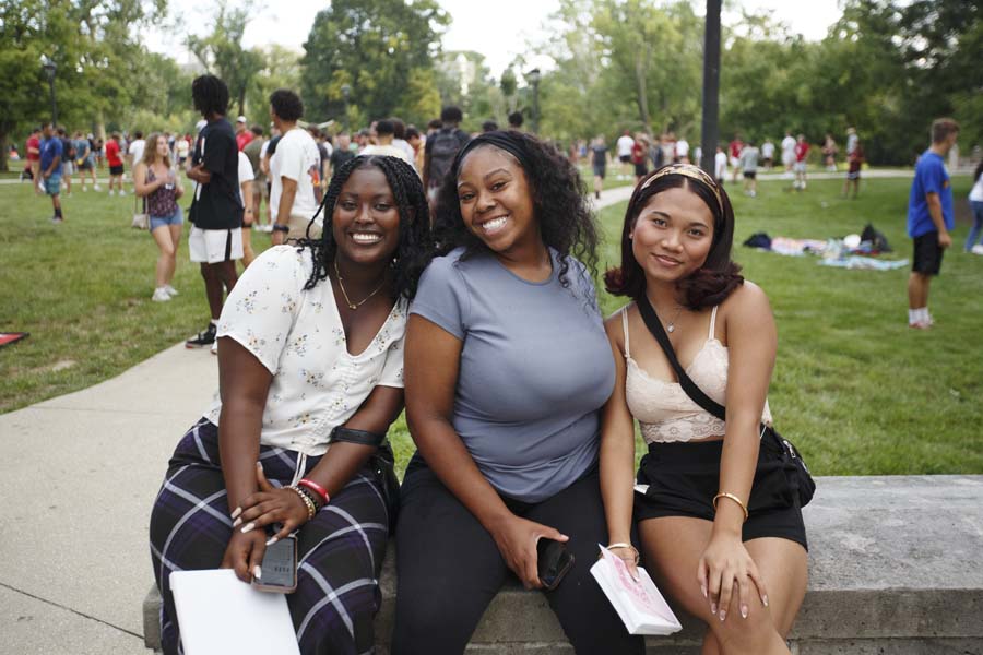 Three students at an outdoor gathering smile at the camera 